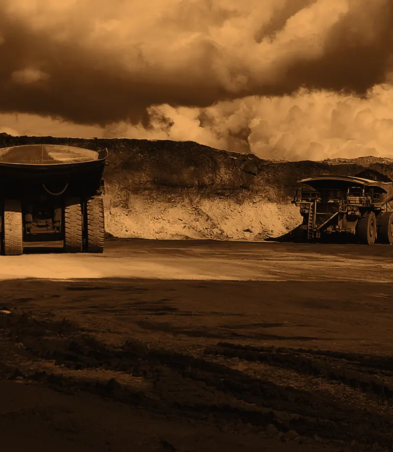 Two haul trucks on an open-pit mine floor under storm clouds